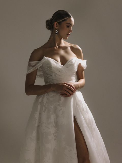 Unser Josephine-Kleid besteht aus wunderschön strukturiertem Jacquard und Blumenorganza.
Es verfügt über ein Korsett-Mieder, während eine skulpturierte Schulter einen Retro-Herz-Ausschnitt bildet und das Dekolleté einer Braut anmutig hervorhebt.
Eine eingeschnittene Taille führt zu einem vollen A-Linienrock, ergänzt durch einen hohen Schlitz, der die Beine betont.
Taschen verleihen einem Hauch von modernem Spaß, während eine Spur von Kunstperlenknöpfen anmutig über die Länge des Zuges fließt und dieses hypnotisierende Kleid vervollständigt, das zeitgenössischen Charme mit zeitlosem Glamour verbindet.